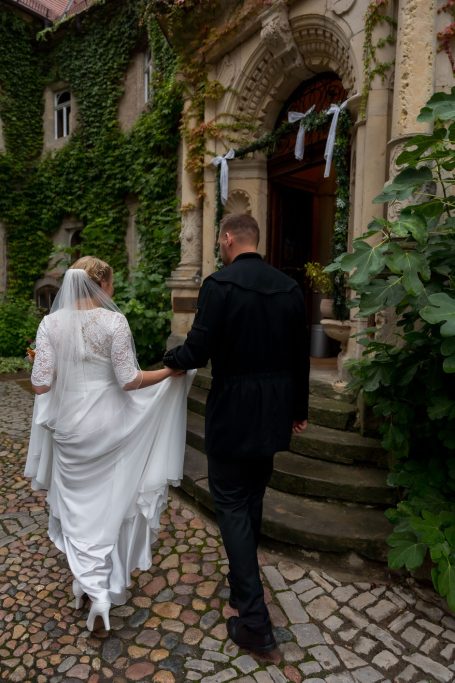 Braut und Bräutigam gehen zur Eingangstür einer historischen, mit Pflanzen bewachsenen Villa.