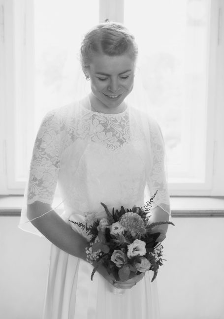 Braut in einem weißen Kleid mit Blumenstrauß, lächelnd und nach unten blickend.