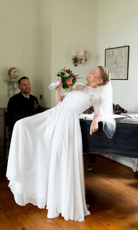 Braut in weißem Kleid hält einen Blumenstrauß und lehnt sich entspannt zurück.