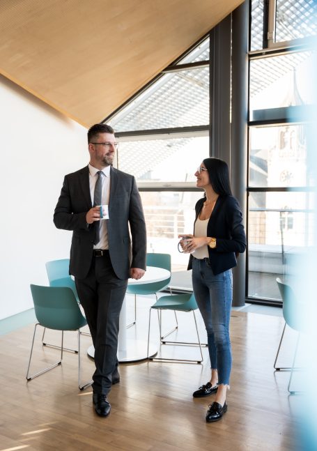 Zwei Personen in einem modernen Büro, im Gespräch, eine hält eine Tasse in der Hand.