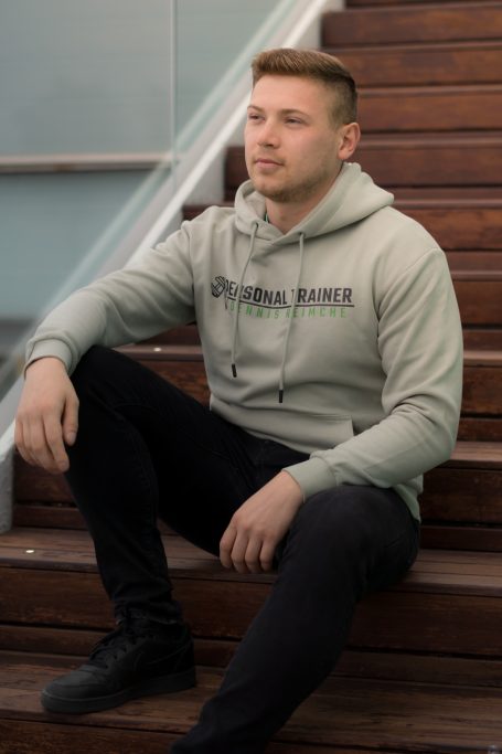 Mann in grauem Hoodie sitzt auf einer Treppe und schaut nachdenklich.