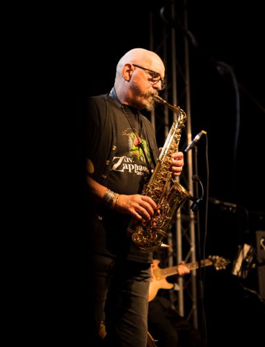 Ein Mann mit Brille spielt Saxophon auf einer Bühnenaufführung.