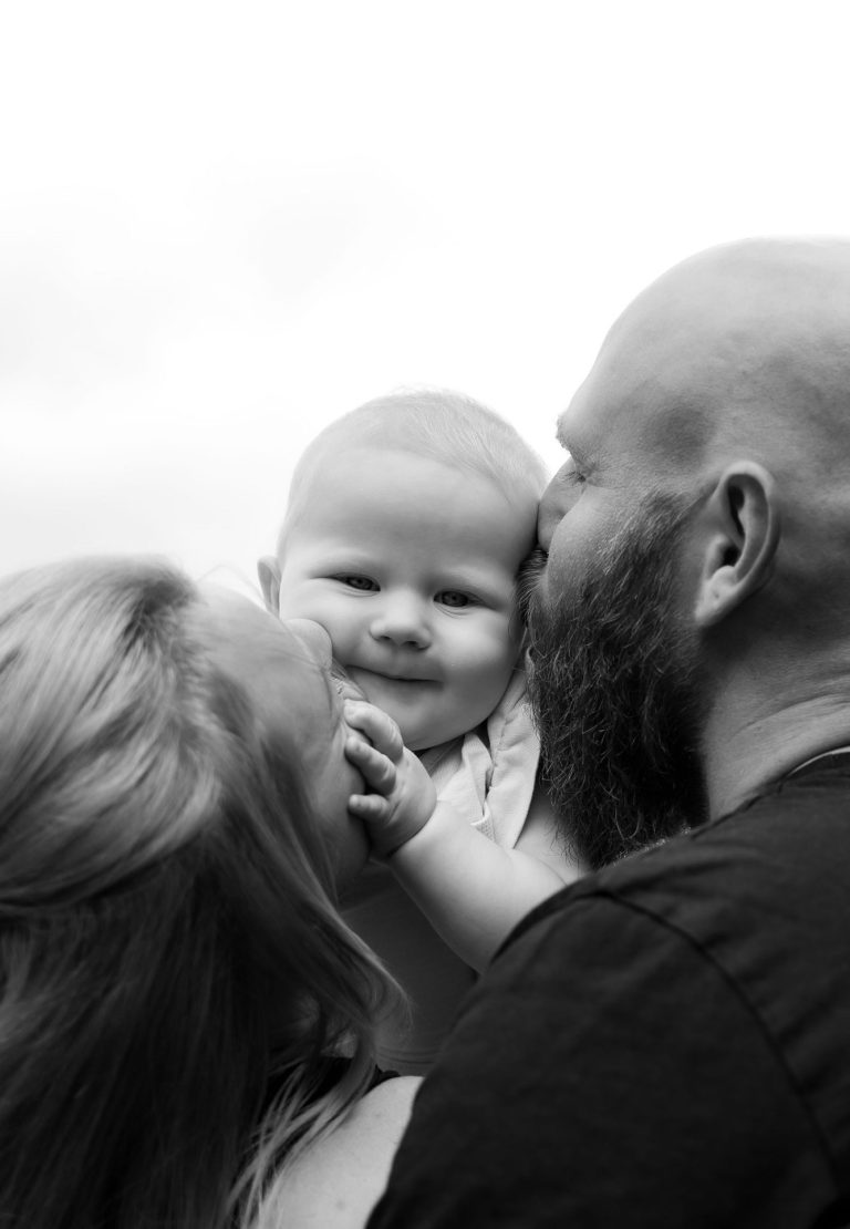 Eine Familie mit einem Baby, das zwischen den Eltern gehalten wird. Alle lächeln.