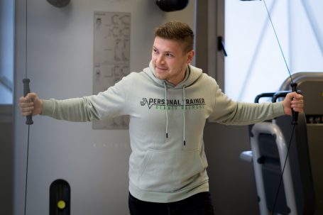 Junger Mann mit Trainingsgeräten, der lächelt und Übungen ausführt.